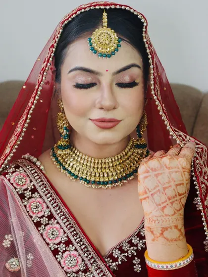A close-up of a bride in a deep red velvet outfit. The makeup features a soft, diffused eyeshadow look with a hint of shimmer.