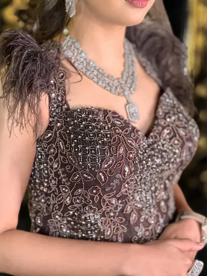 A close-up of the exquisite beadwork and feather shoulder detail on our wine-colored fish-cut gown.