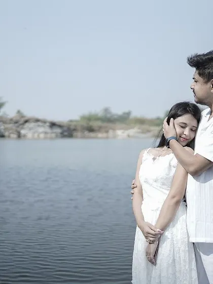 A tender embrace by a lake, with the groom gently holding the bride, both looking out at the serene landscape.