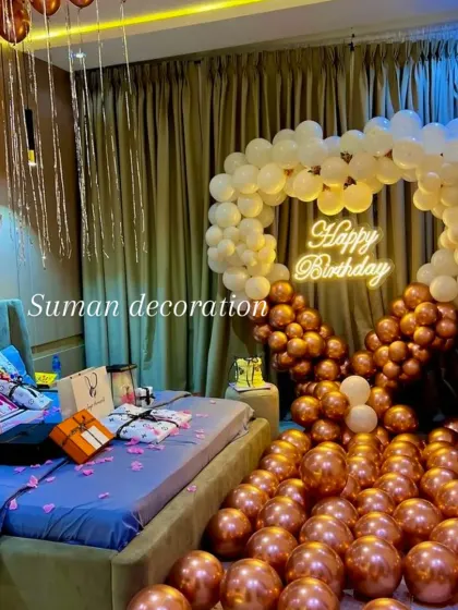 A romantic birthday surprise set up in a bedroom. This features a heart-shaped balloon arch in white and chrome gold, a neon sign, and balloons covering the floor.