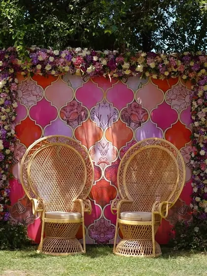 A cozy and photogenic seating area for the bride and groom. We used a backdrop with a vibrant Moroccan tile print, framed by a lush border of flowers, and paired it with traditional peacock chairs.