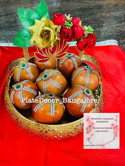 Pomegranates decorated with rhinestone strips and green kundan stones in a golden basket, topped with artificial flowers.