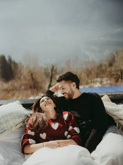Laughter and love on a cozy, pillow-filled deck overlooking the mountains. This photo captures the playful and comfortable connection between the couple during their romantic retreat.