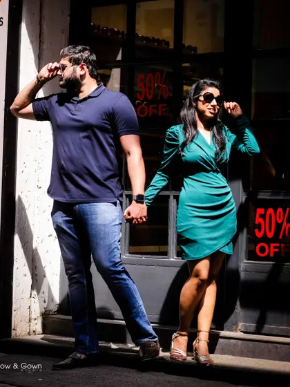 A stylish and fun pre-wedding photo with the couple striking a pose against a storefront. The strong sunlight creates dramatic shadows, adding an editorial feel to the shot.