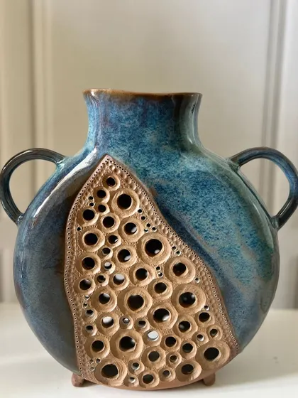 This large, slab-built vase has a beautiful contrast between the smooth blue glaze and the unglazed, pierced section.