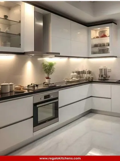 This high-gloss white L-shaped kitchen is bright and modern. The black countertop and integrated appliances provide a sharp contrast, while glass-front cabinets offer a place to display your favorite dishware.