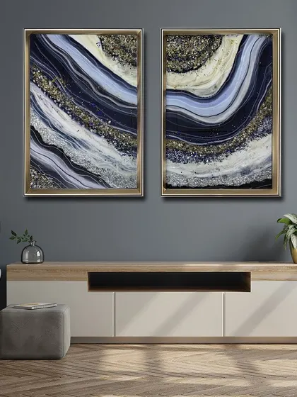 A beautiful set of two resin art paintings in deep blue, white, and gold. The wave-like patterns are filled with glittering crystals, perfect for creating a sophisticated and cohesive look above a console.