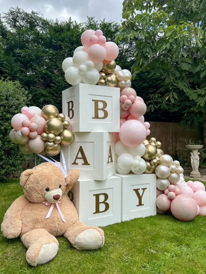 A charming outdoor baby shower setup with giant "BABY" blocks, a large teddy bear, and a pink and gold balloon arrangement. It's a sweet and classic theme.