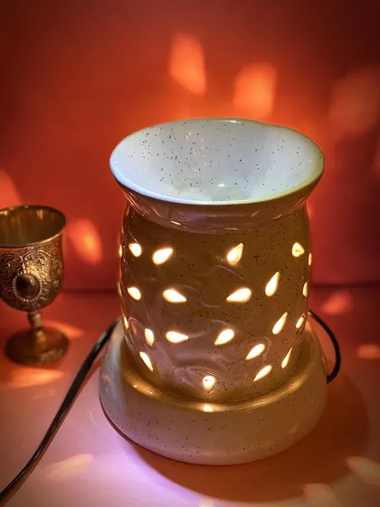 Our electric aroma diffuser creates a warm, inviting glow while filling your room with a relaxing scent. This model features a speckled ceramic finish and teardrop cutouts, casting beautiful light patterns that enhance the calming atmosphere.