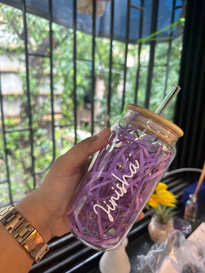 Holding up the personalized 'Jinisha' sipper to show how it looks against a natural background. The purple shredded paper inside adds a nice touch for gifting.