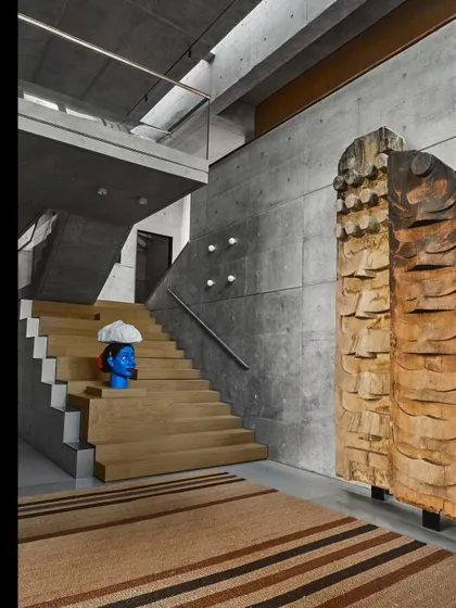 The main staircase in a Delhi residence, crafted from wood and set against a backdrop of exposed concrete. The space is designed as a gallery for art, integrating it directly into the home's architecture.
