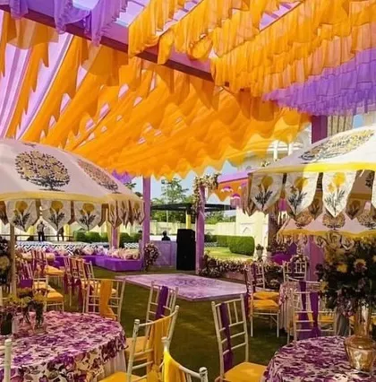 The guest seating area at a vibrant Mehendi event. The decor features printed tablecloths and custom-designed umbrellas, all in a cohesive purple and yellow color scheme.