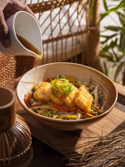 Pouring a savory sauce over a fish and noodle bowl. This action shot adds a dynamic element to the dish.