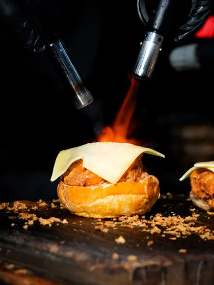 A different angle of the blowtorch in action, highlighting the melting cheese and the intense heat used to create the perfect finish.