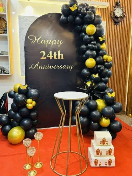 I can create a sophisticated and modern theme for any anniversary. This 24th-anniversary decoration uses a sleek black and gold color palette, with a custom-printed arch backdrop and a cascading balloon garland for a chic and stylish celebration.