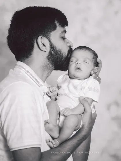 A tender black and white moment of a father kissing his sleeping newborn's forehead. This classic portrait is full of love and peaceful emotion.