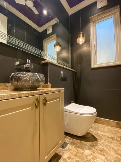 This powder room at C-926 features a unique stone-carved vessel sink, a dark, moody color palette, and elegant pendant lighting for a truly custom feel.