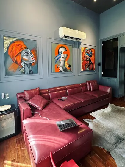 A bold and artistic TV lounge featuring a deep red leather sectional sofa. The wall is adorned with vibrant portraits set within classic molding, creating a gallery-like feel.