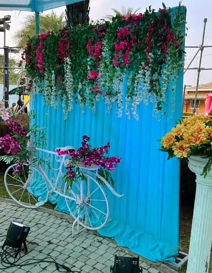 A charming photo booth created for the Haldi ceremony, featuring a decorated bicycle against a blue backdrop with hanging flowers.