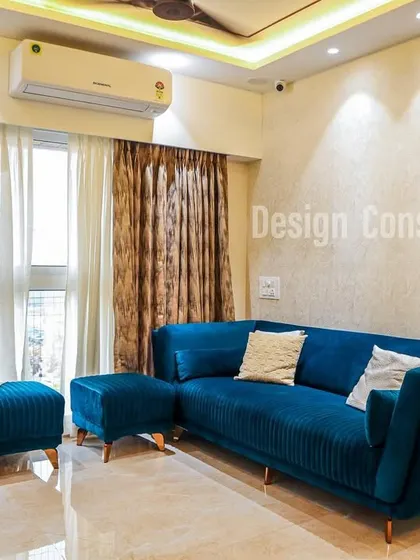 A comfortable and stylish living room featuring a plush teal blue L-shaped sofa. The space is kept bright and airy with light-colored walls and sheer curtains, allowing the sofa to be the main pop of color.