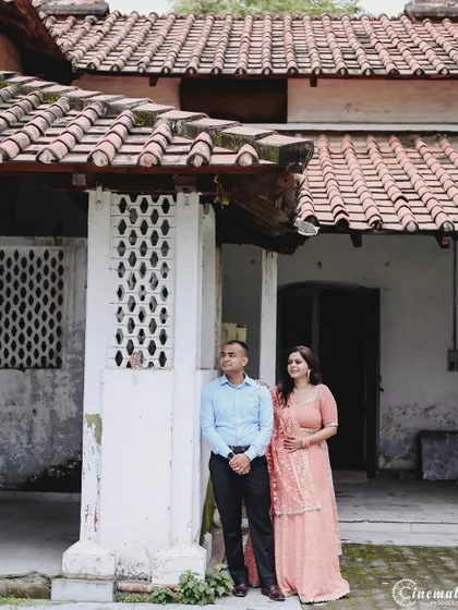 A quiet, observational shot of a couple standing outside a rustic house. Even in a more formal pose, their relaxed posture and connection feel authentic and unforced.