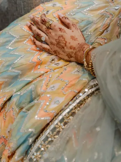 The texture and detail of a lehenga. This close-up on the bride's hand against the fabric highlights the beautiful craftsmanship of her outfit.