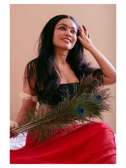 An artistic portrait featuring a peacock feather. The composition and the subject's expression create a sense of connection to nature and a quiet, meditative mood.