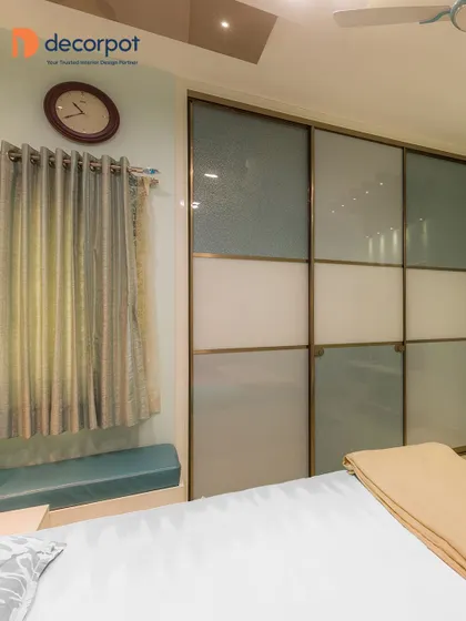 A multi-panel sliding wardrobe with a mix of textured and frosted glass in a cool blue and white palette. The design is complemented by a built-in bay window seating area for a cozy reading nook.