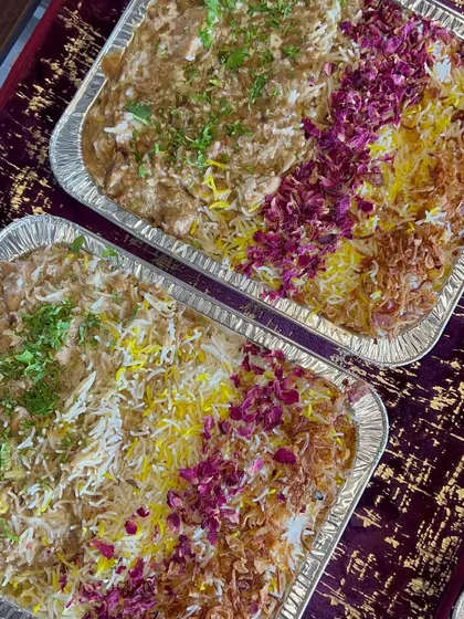 Two large foil trays filled with my signature biryani, garnished with saffron rice, fried onions, and rose petals, ready for a large event.