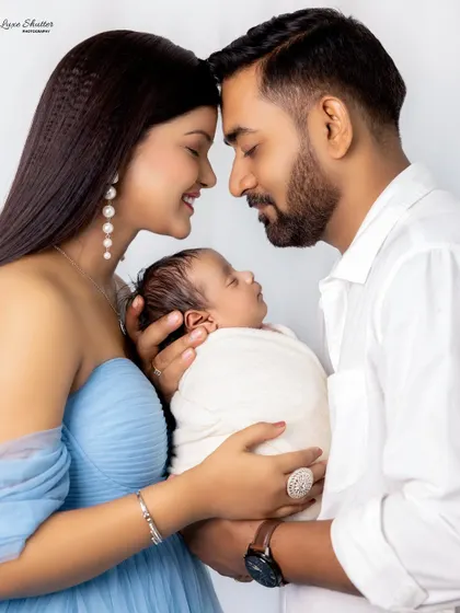 A classic and intimate portrait of new parents, their heads touching as they cradle their newborn. The image is filled with love and serenity.