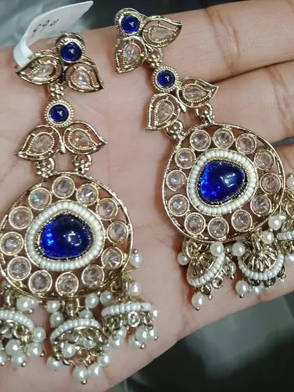 These blue and gold jhumka earrings are a beautiful blend of colour and tradition. The blue stone is the highlight, complemented by the classic jhumka design with pearl drops.