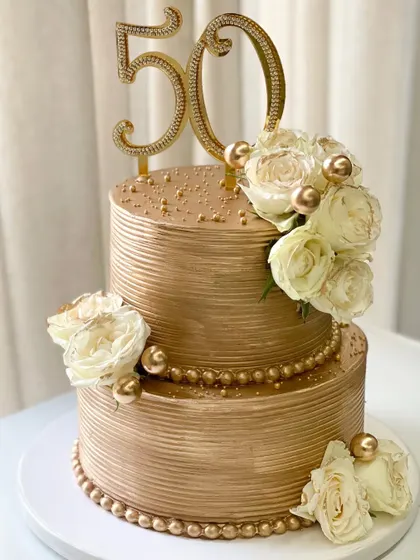 Another view of my signature golden tiered cake, customized for a 50th birthday. The smooth, ribbed ganache finish provides the perfect canvas for the floral arrangements.