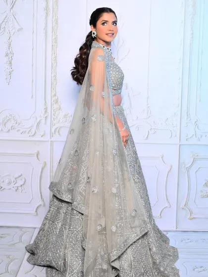 An elegant reception look in a silver-grey lehenga. The makeup features a cool-toned smokey eye and a chic ponytail, creating a sophisticated and modern bridal style.
