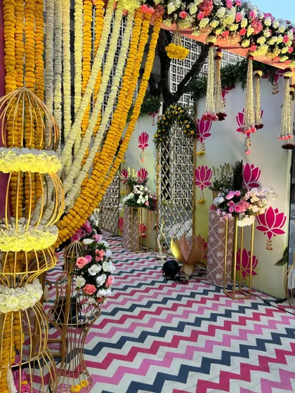 A modern take on Mehendi decor, this entrance features a vibrant pink, black, and white chevron carpet, flanked by traditional marigold strings and contemporary floral arrangements.