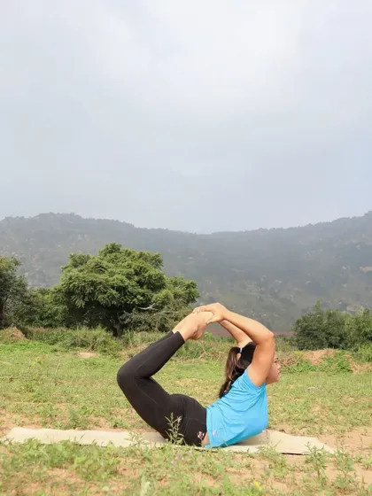 Dhanurasana (Bow Pose) in a grassy field, connecting with the earth while opening the heart.