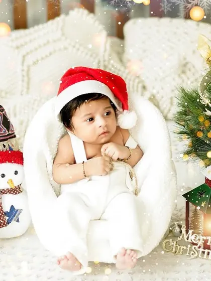A cute baby boy in a white outfit and Santa hat, sitting in our winter wonderland studio setup. We have a variety of props to create your perfect Christmas portrait.