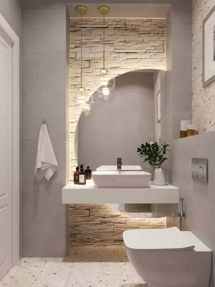 This powder room is small but stylish. The floating white vanity and toilet create a sense of space, while the textured stone accent wall and pendant lights add a touch of drama and luxury.