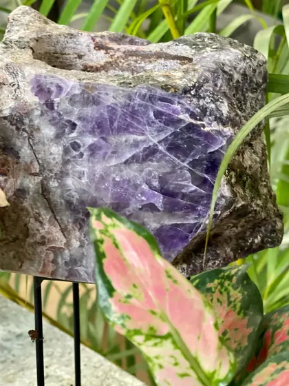 A close-up of an amethyst crystal planter on its stand. The deep purple hues and raw texture of the crystal make this a stunning and unique holder for a small plant or candle.