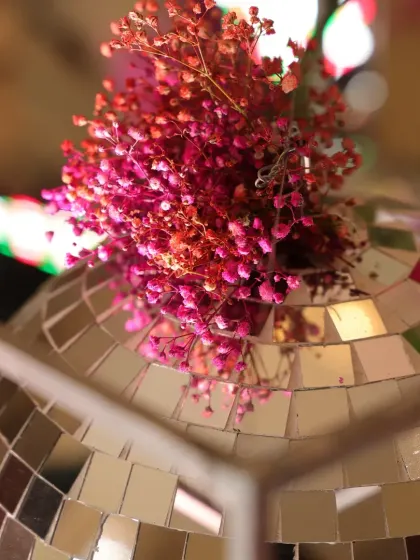A macro shot of a disco ball topped with delicate dried pink flowers, highlighting the small, thoughtful details of the decor.