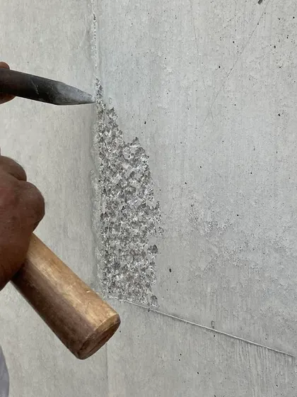 A craftsman applying a bush-hammered finish to a concrete surface. This technique uses a specialized hammer to texturize the concrete, exposing the aggregate within.