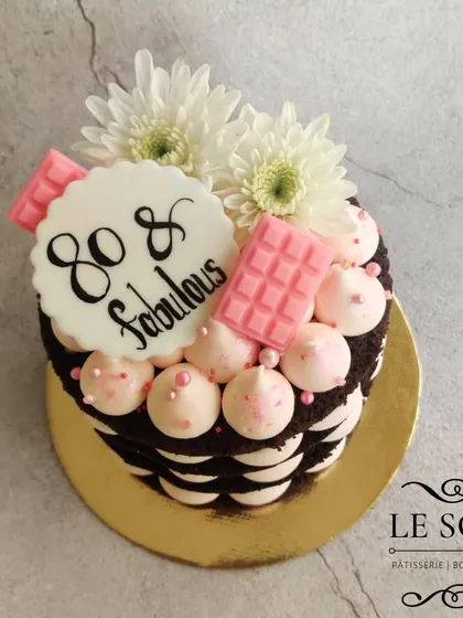 A semi-naked cake for an 80th birthday. This half-kg chocolate cake is layered with pink-tinted cream cheese frosting and decorated with ruby chocolate and fresh flowers.