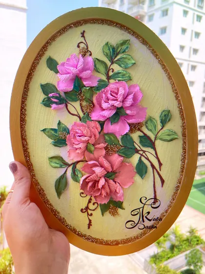 An elegant oval wall panel featuring a bouquet of pink roses on a soft yellow background, framed in gold.