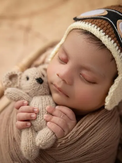 A close up of our tiny pilot, cuddling a teddy bear. This shot focuses on the baby's peaceful expression and the adorable details of the hand knit aviator hat.