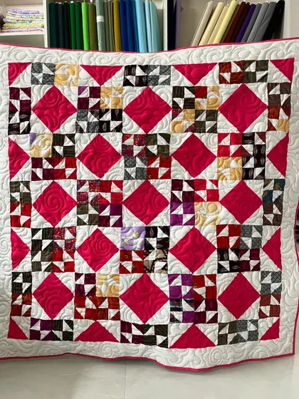 A vibrant and scrappy quilt featuring a complex star pattern. The bright pink diamonds give it a cheerful energy.
