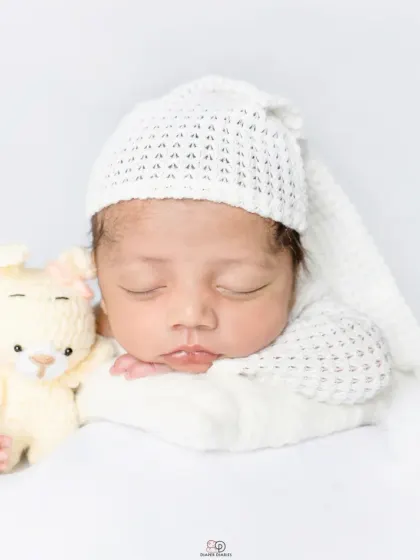 A pure and simple newborn portrait against a clean white background. The baby is dressed in a white knitted outfit and sleepy hat, showcasing their angelic features.