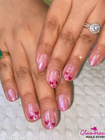 A sweet and shimmery design with a pearlescent pink base and accent nails featuring a scattering of tiny, hand-painted red hearts.