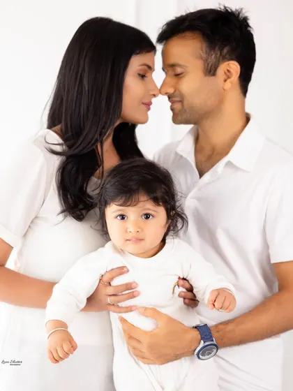 A loving family portrait with the parents looking at each other while holding their baby. The focus is on their connection as a new family.