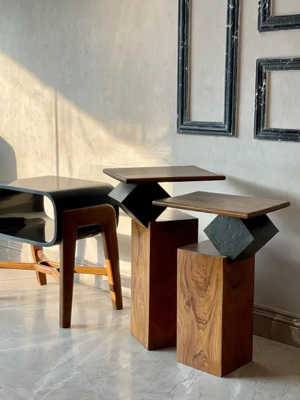 Our accent tables catching the sunlight. This image features the "Roll The Dice" nesting tables, which combine wooden pedestals with stone cubes, and the sleek "Plain Jane" side table with its black top and wooden legs.