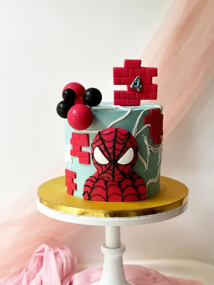 This Spider-Man cake features a bold, graphic look with a 3D mask emerging from the side. The design includes fondant brick details and balloon accents for a modern take on the superhero theme.