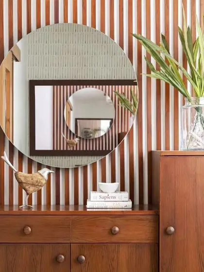 This wall features vertical wood battens, creating a fluted effect that adds texture and visual interest. The round mirror provides a soft contrast to the linear pattern.